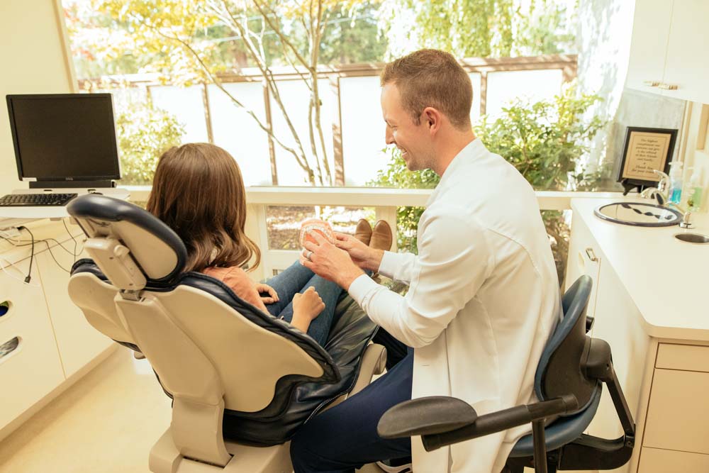 Dr. Nick Forsythe holds a model of teeth while speaking to a dental patient who is seated in an exam chair
