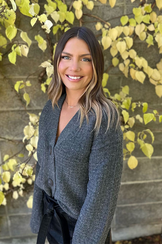 Headshot of Desiare wearing a gray sweatshirt. The background is a wall with vibrant green and yellow leaves and a serene atmosphere.