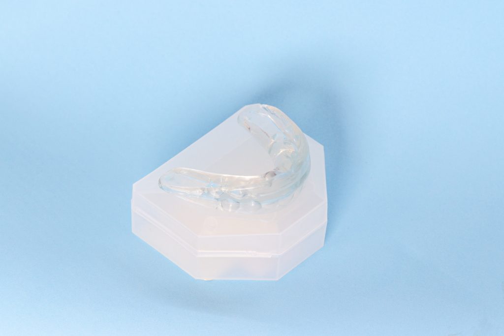 A clear mouth guard sitting on a white protective case on a blue background