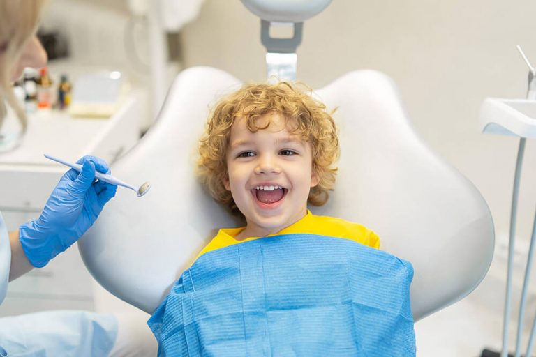 A young boy sits in a dental exam chair at a pediatric dentistry checkup to ensure healthy teeth
