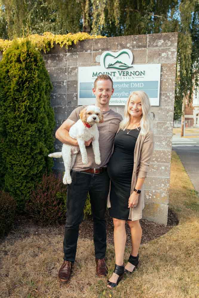 Drs. Nick and Whitney Forsythe stand near a sign for their dental practice with their dog