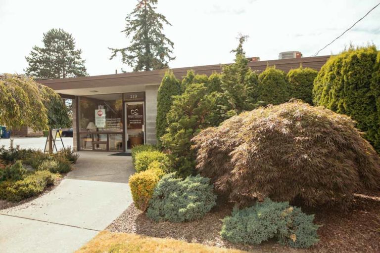 The image showcases the exterior of Mount Vernon Smile Design, surrounded by greenery and displaying its operating hours.