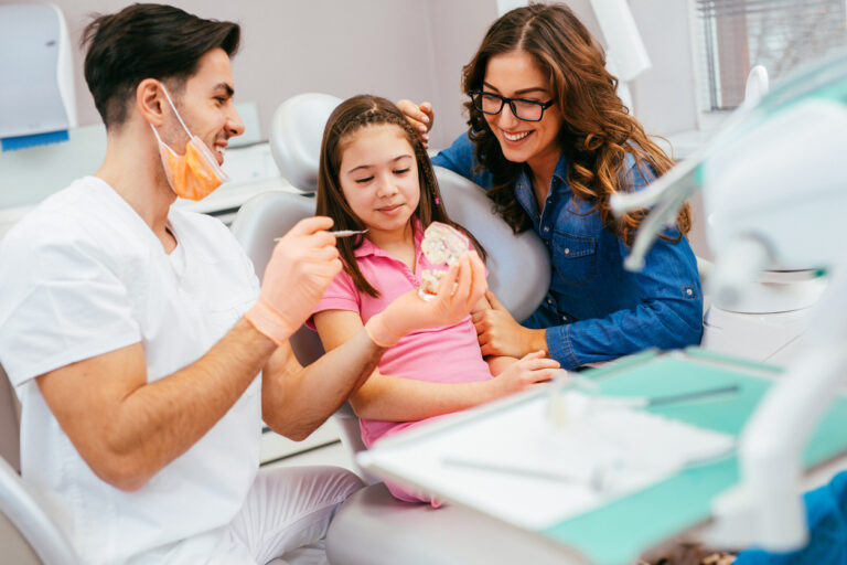 child in dental chair with parent and dentist next to the chair